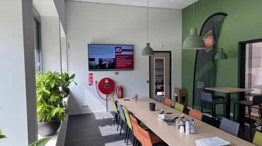 Kantine met tafels en stoelen en aan de wand een scherm.